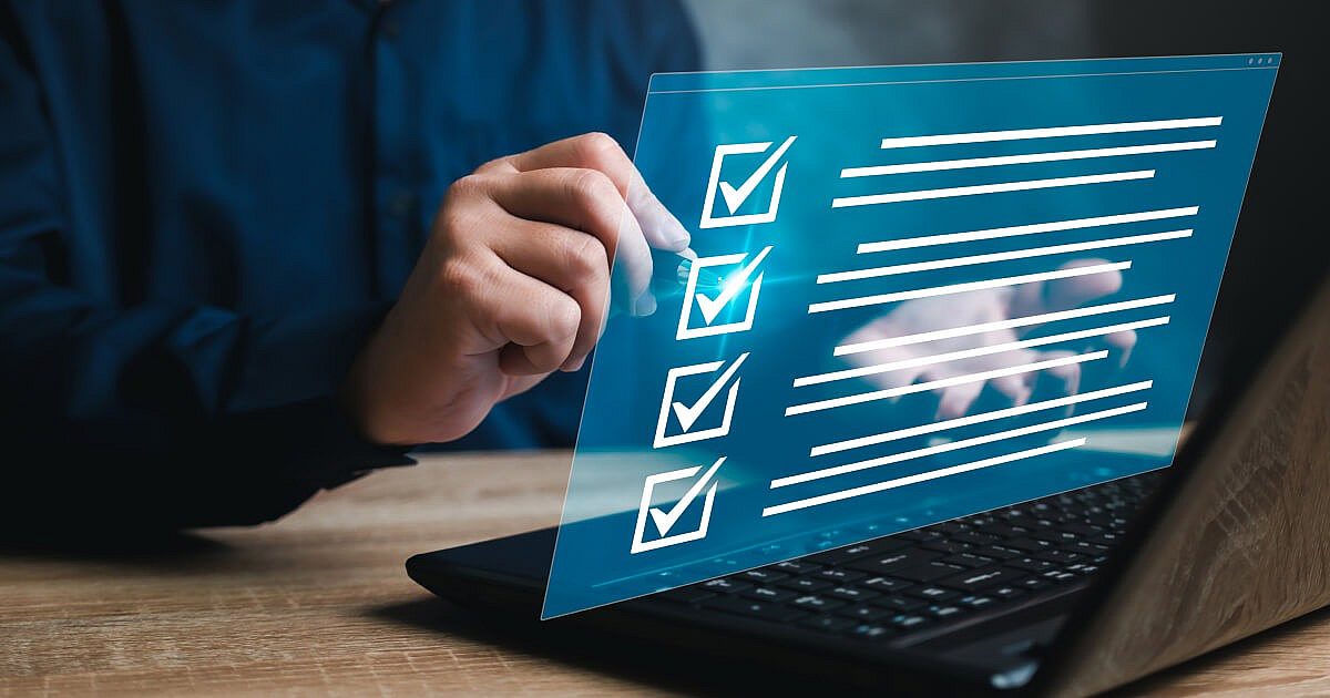 A photo of a man with a checklist on his computer in front of him.